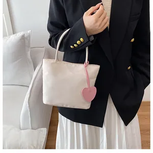 Detail of a silky cream tote bag with a pink heart charm held by a model in a suit