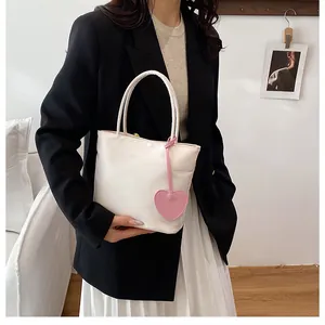 Minimalist white tote bag with pink heart charm shown styled with casual chic outfit
