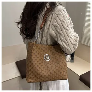 Close-up of brown tote bag with M-letter pattern and silver chain shoulder strap
