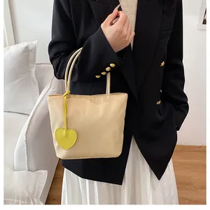Close-up of beige nylon tote bag featuring a bright yellow heart charm and thin handles