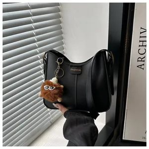 Close-up of black leather bucket bag with a cute brown plush monster charm and fashion label