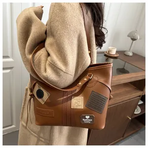 Detailed view of brown PU leather tote bag with vintage patches and side tassel accents