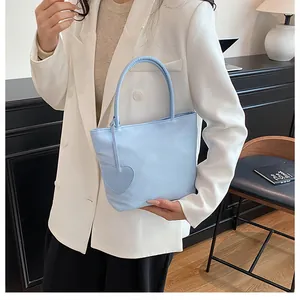 Close-up of light blue minimalist tote bag with heart charm accessory on white blazer