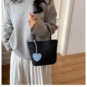 Detail of black nylon tote bag featuring a light blue heart pendant and zipper closure