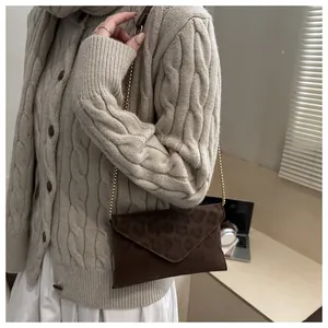 Brown leopard print envelope bag with gold chain strap shown in a modern lifestyle setting