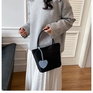 Detail of minimalist black tote bag featuring a light blue heart-shaped leather charm