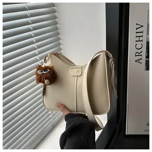 Detail of cream hobo shoulder bag with fuzzy monster pendant and adjustable leather strap