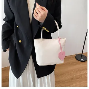 Detailed shot of white tote bag with pink heart pendant on model in black blazer