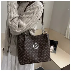 Detail of coffee brown tote bag with metal M logo and silver chain straps in lifestyle setting