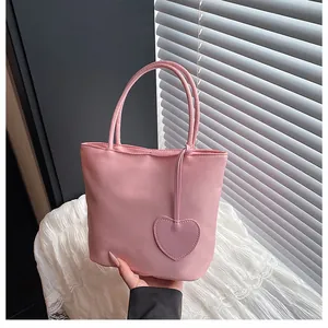 Detailed shot of a pink nylon tote bag featuring a heart charm and smooth satin texture