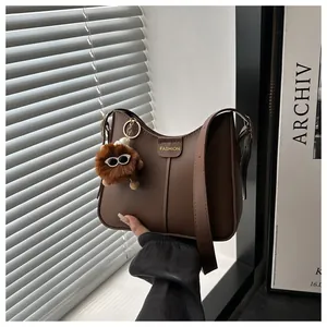 Detail of coffee brown leather bucket bag with gold metal logo and plush monster charm