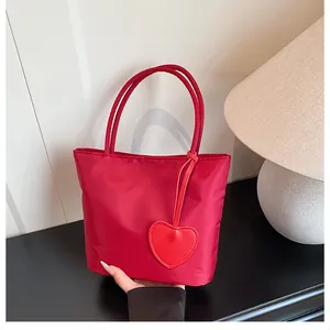 Detail of red nylon tote bag with heart charm against a minimalist home background