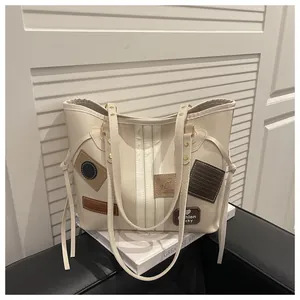 Detail view of cream tote bag featuring brown leather patches and drawstring tassels