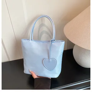 Close-up of light blue nylon tote bag with thin handles and a heart charm detail