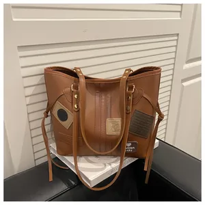 Close-up of brown PU leather tote bag with vintage patches and side fringe details