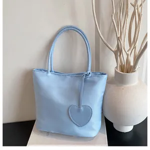 Close-up of light blue nylon tote bag with minimalist heart pendant on a white platform