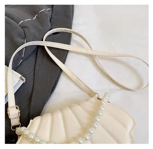 Detail of shell-shaped cream bag with vertical textures and faux pearl chain handle