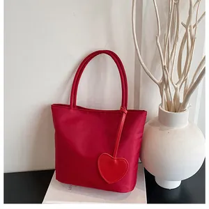 Minimalist red nylon tote bag featuring a heart charm decoration on white display box