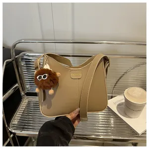Close-up of khaki PU leather bucket bag with fashion label and brown plush ball charm