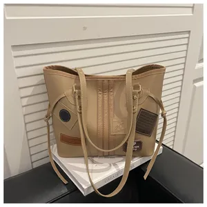 Detail view of khaki PU tote bag with decorative patches and straps on a black chair