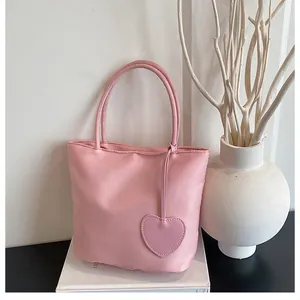Detailed view of pink satin tote bag with heart charm and slim handles on books