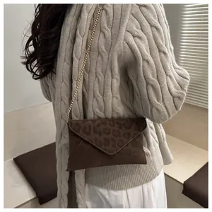 Détail du sac enveloppe à imprimé léopard avec chaîne dorée porté par un mannequin