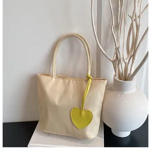 Close-up of beige nylon tote bag featuring a yellow heart-shaped leather pendant detail