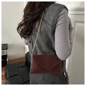 Detail of burgundy leopard embossed envelope crossbody bag with gold chain strap on model