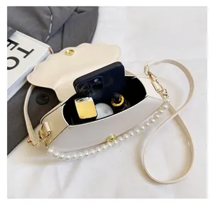 Internal storage detail of shell-shaped crossbody bag with pearl strap and essentials