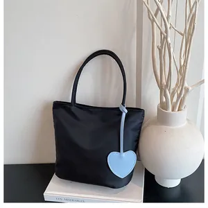 Detail of black waterproof nylon tote bag with a light blue heart leather charm accessory