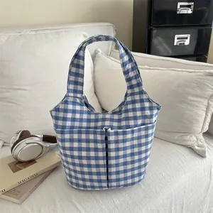 Blue and white checkered canvas tote bag with two front pockets on a sofa
