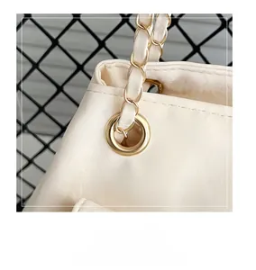 Détails de la boucle dorée et de la bandoulière en chaîne de cuir sur un sac crème