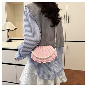 Detail of pink shell crossbody bag featuring pearl handle and adjustable shoulder strap