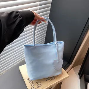 Sky blue minimalist tote bag with heart pendant accessory shown in a modern lifestyle setting
