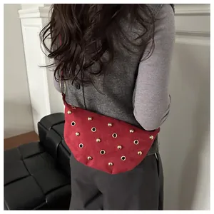 Detalle del bolso bandolera de ante rojo con tachuelas doradas y ojales metálicos