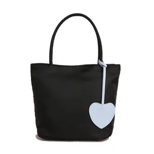 Minimalist black nylon tote bag with blue heart pendant shown in a center-aligned front view