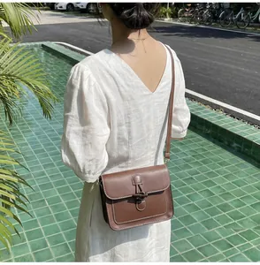 Close-up of retro brown leather crossbody bag with white stitching and horn toggle detail