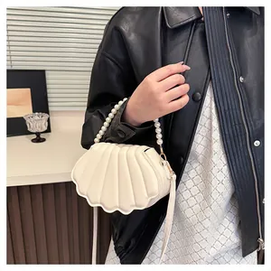Detail of shell-shaped crossbody bag with pearl handle and beige pleated texture leather