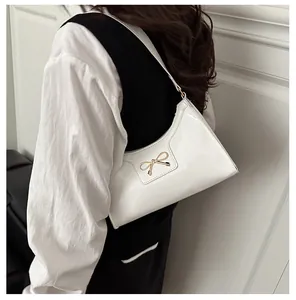 Detail of white glossy leather baguette bag with a gold metal bow on a model