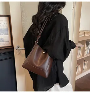Detail showing the large dark brown leather bucket bag worn as a shoulder tote by a model