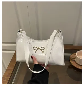 Detail of the white patent leather baguette bag with a stylish golden bow metal buckle
