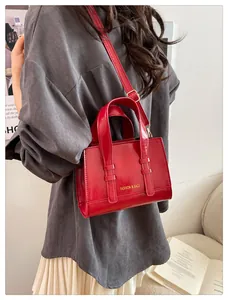 Detail of red glossy patent leather handbag with gold hardware and removable shoulder strap