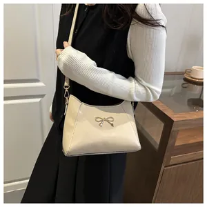 Detail of a creamy white crossbody bag with a gold bow buckle on a lifestyle background