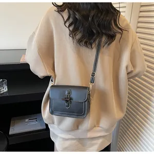 Detail of black leather crossbody bag with white stitching and metal buckle on a model