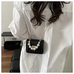 Detail of black woven mini crossbody bag with pearl handle and gold chain on white shirt