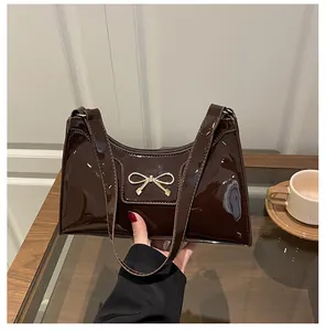Close-up of dark brown patent leather baguette bag with a golden bow metal clasp