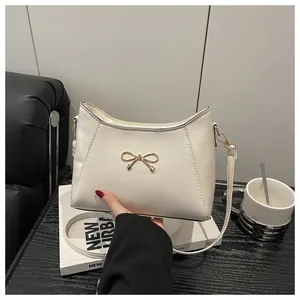 Detail of white PU leather shoulder bag with elegant golden bow metal ornament