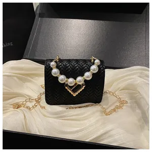 Detail of black woven mini bag featuring pearl handle and gold heart clasp in gift box