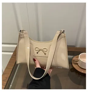 Detail of glossy beige bow baguette bag with polished gold hardware and thin straps