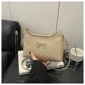 Detail view of cream shoulder bag featuring an elegant gold bow buckle and smooth leather texture